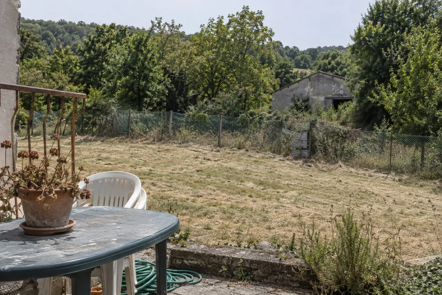 Terrasse de riverain dominant les clôtures rouillées et les bâtiments abandonnés du zoo fermé des Trois Vallées, dans le Tarn
