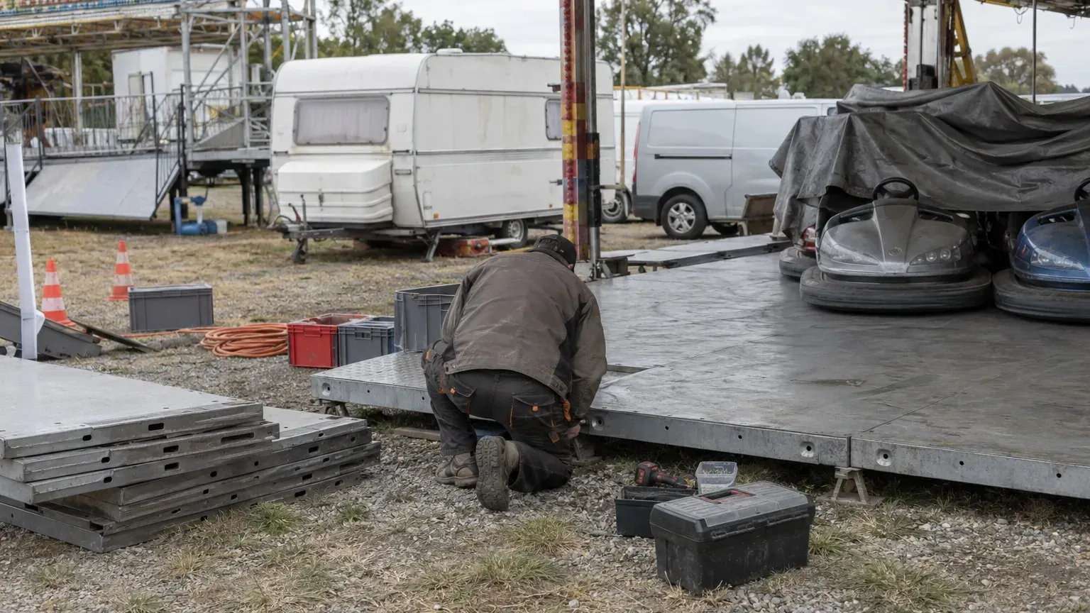 Forain de dos montant les plaques d'une piste d'autos tamponneuses vide sur un champ de foire, caravane en arrière-plan