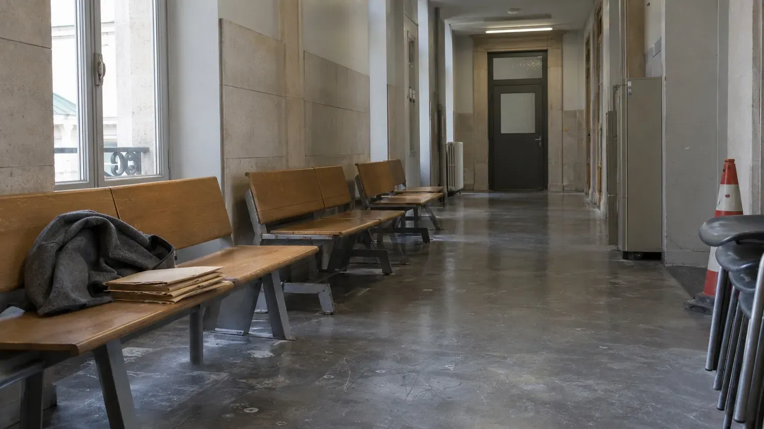 Couloir désert du tribunal de Paris avec bancs en bois usés et porte close le matin